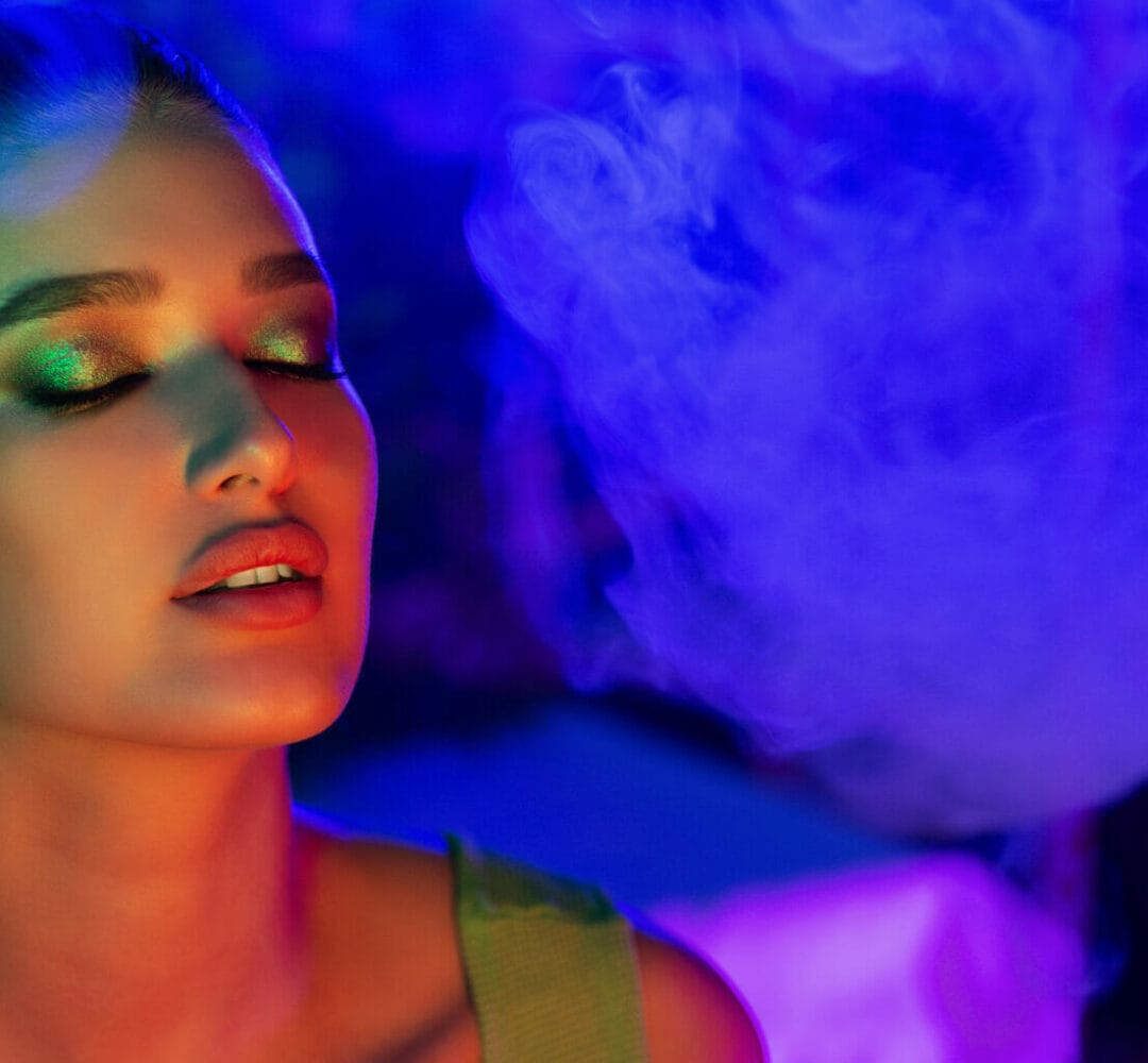 Young woman smoking vape in neon blue light